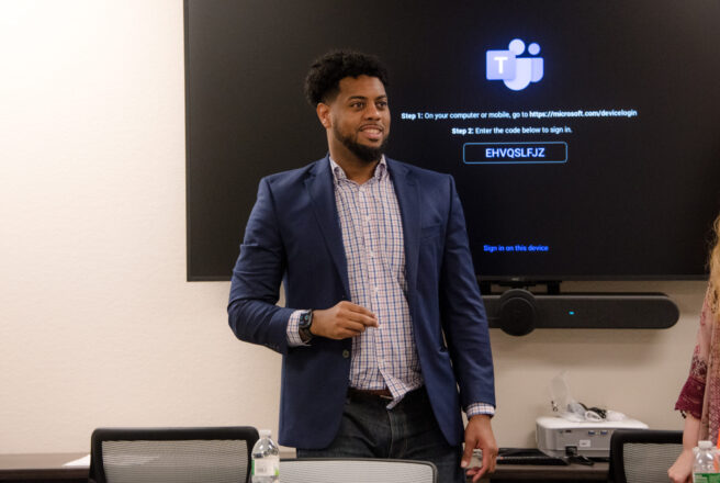 A male presents in front of a monitor in a conference room