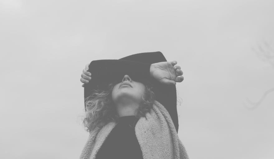 Shot of woman standing with the sky behind her, with both arms covering her eyes