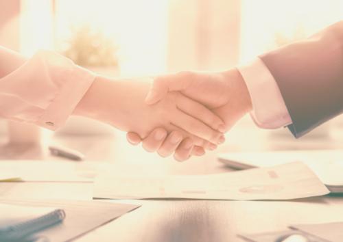 A closeup image of a woman's hand and man's hand shaking, both in business attire