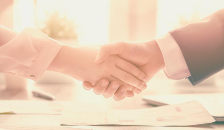 A closeup image of a woman's hand and man's hand shaking, both in business attire