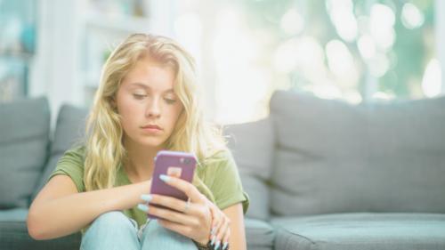 A young adult with long blonde hair, looking at their cell phone