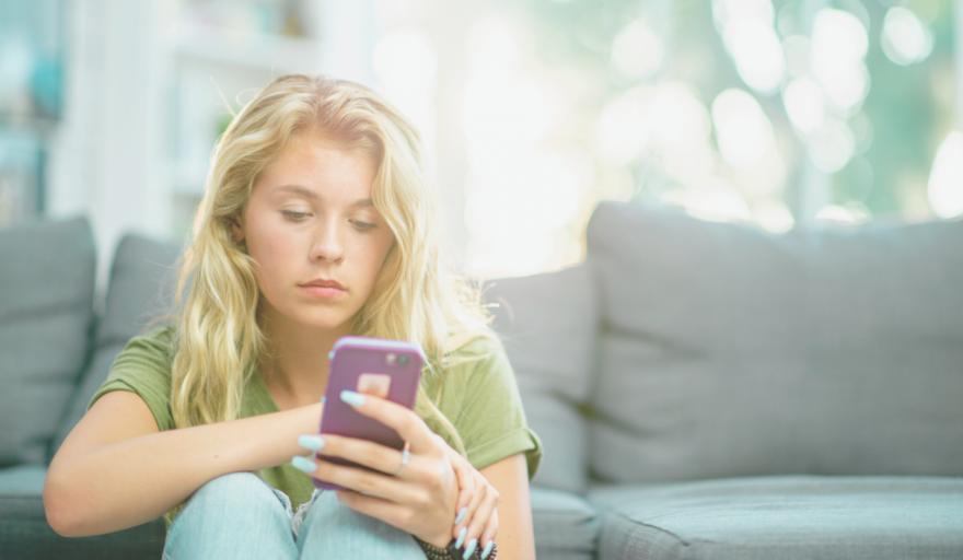 A young adult with long blonde hair, looking at their cell phone