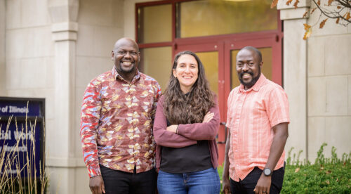 Flora, Moses and Joshua stand together outside of a building and smile