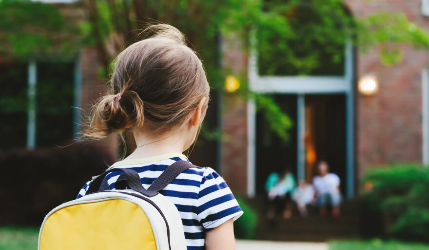 back of child returning home, wearing yellow backpack